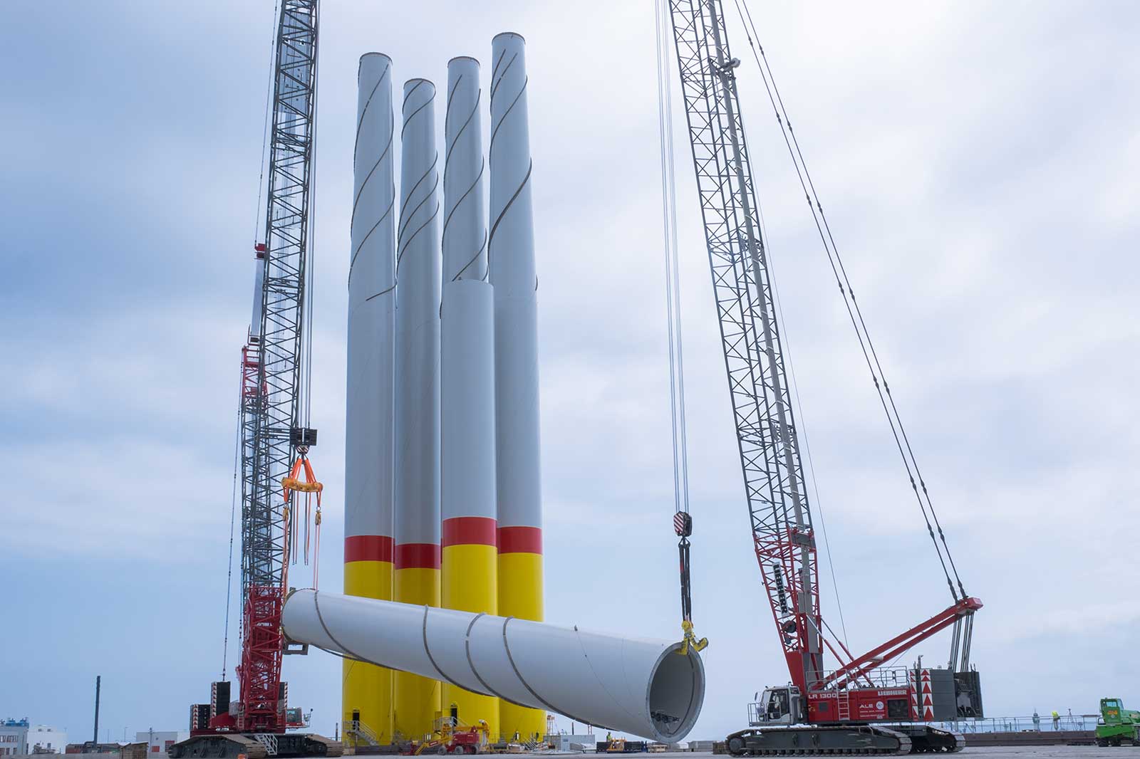 A construction site with tall wind turbine components and cranes preparing to assemble them for wind energy generation.