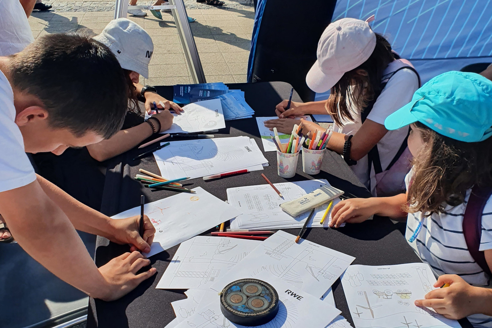 Children are drawing on paper with coloured pencils at a table, with RWE materials and a decorative item on the table.