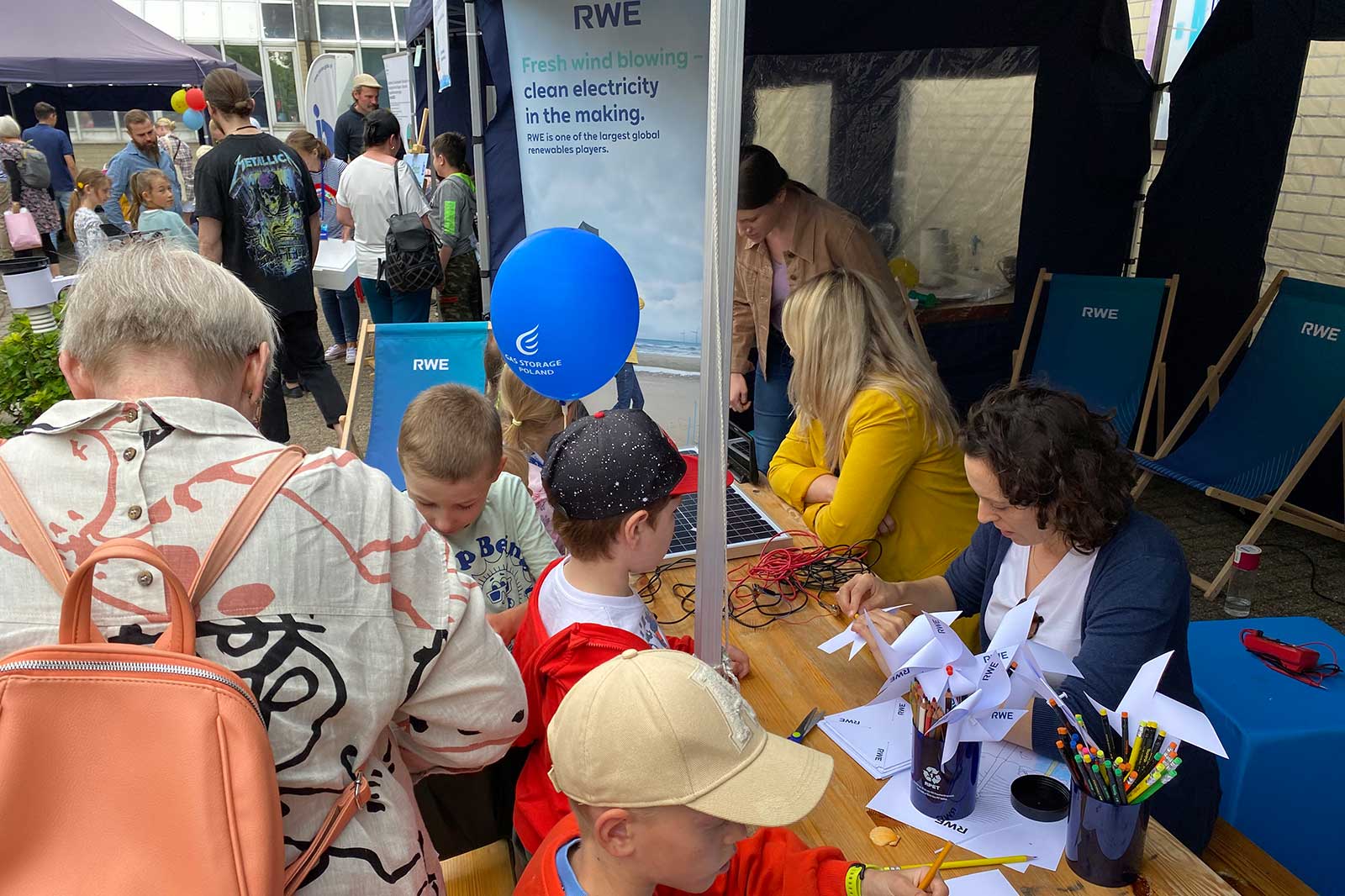 A busy event booth with families engaging in activities. A banner displays RWE's commitment to renewable energy.