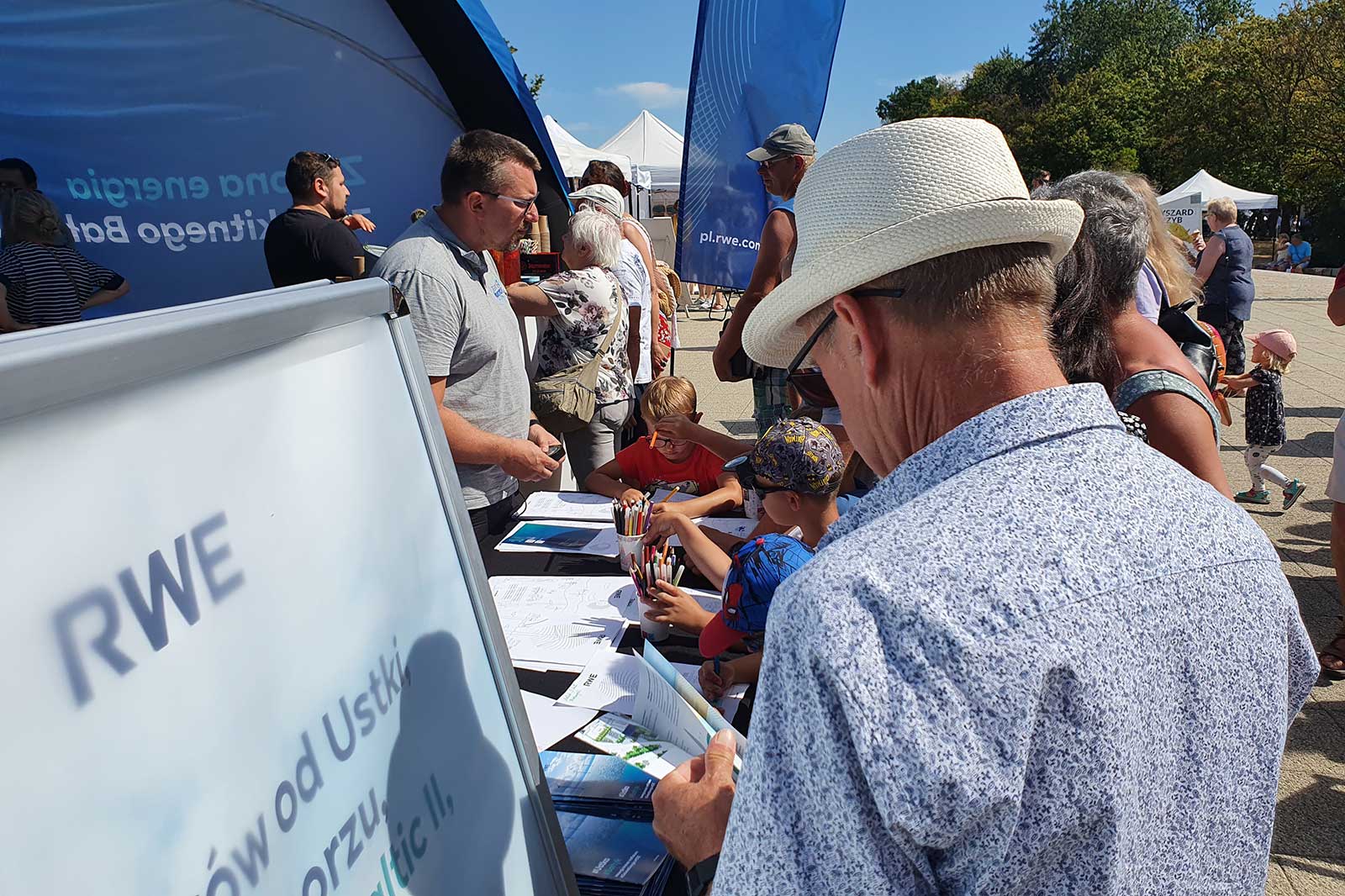 A group of people engaging at a booth display with RWE branding. Children are drawing while adults interact with staff.
