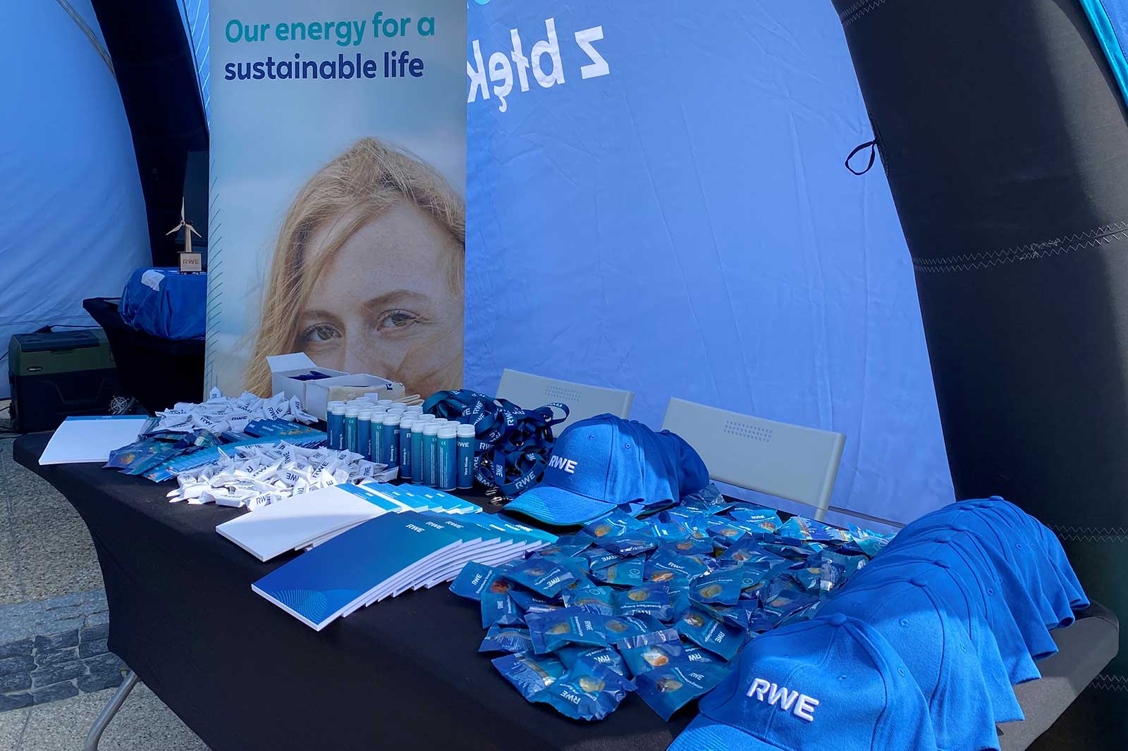 A display featuring promotional items including blue hats and pins with RWE branding, alongside brochures under a tent.
