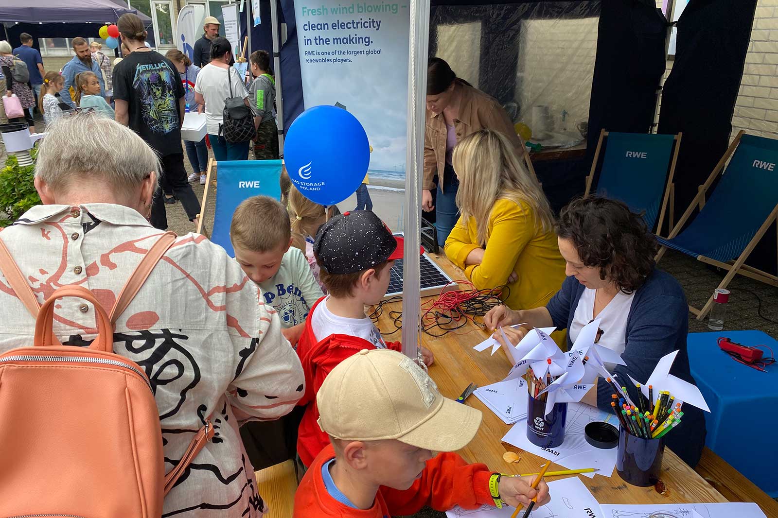 A crowded event with children engaging in activities at a booth promoting renewable energy with windmills and colourful balloons.