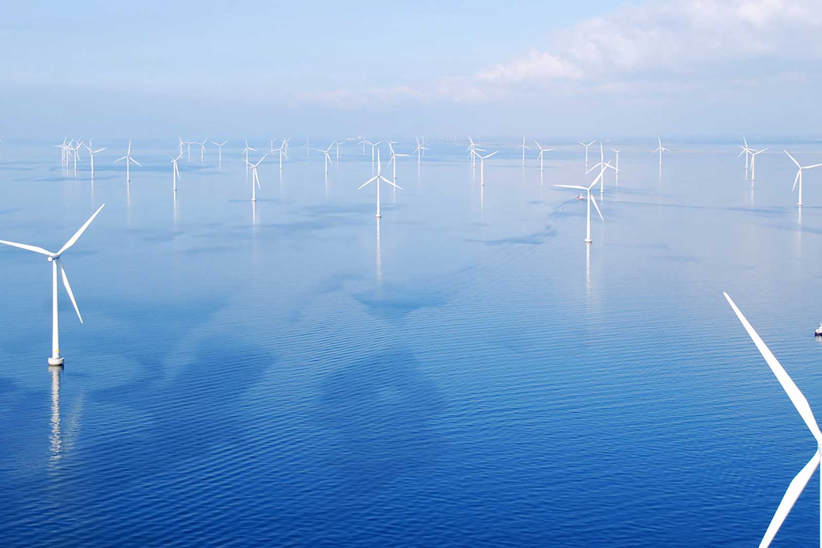 Aerial view of offshore wind turbines on calm blue waters under a clear sky.