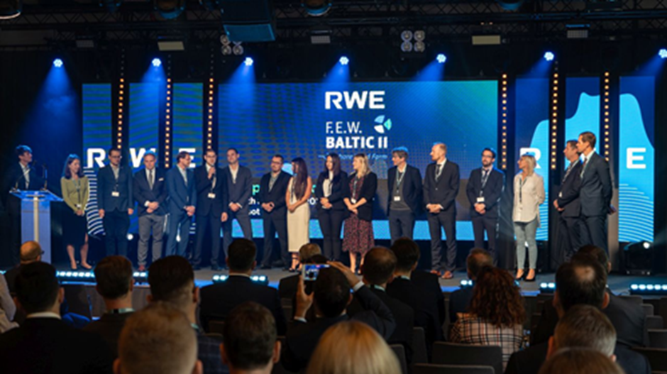 A group of professionals gathered on stage for the RWE F.E.W. Baltic II event, with blue lighting and a large screen in the background.